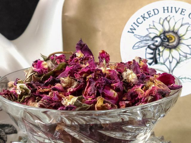 Dried rose buds heaped in a cut-glass bowl beside a Wicked Hive Garden kraft pouch.